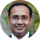 A smiling man with black hair and glasses.